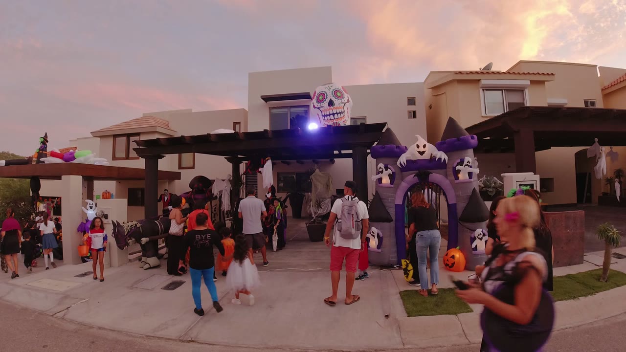 Children and adults move closer to the purple haunted entrance in Los Cabos, Mexico, with pumpkins and ghost figures beside the doorway.