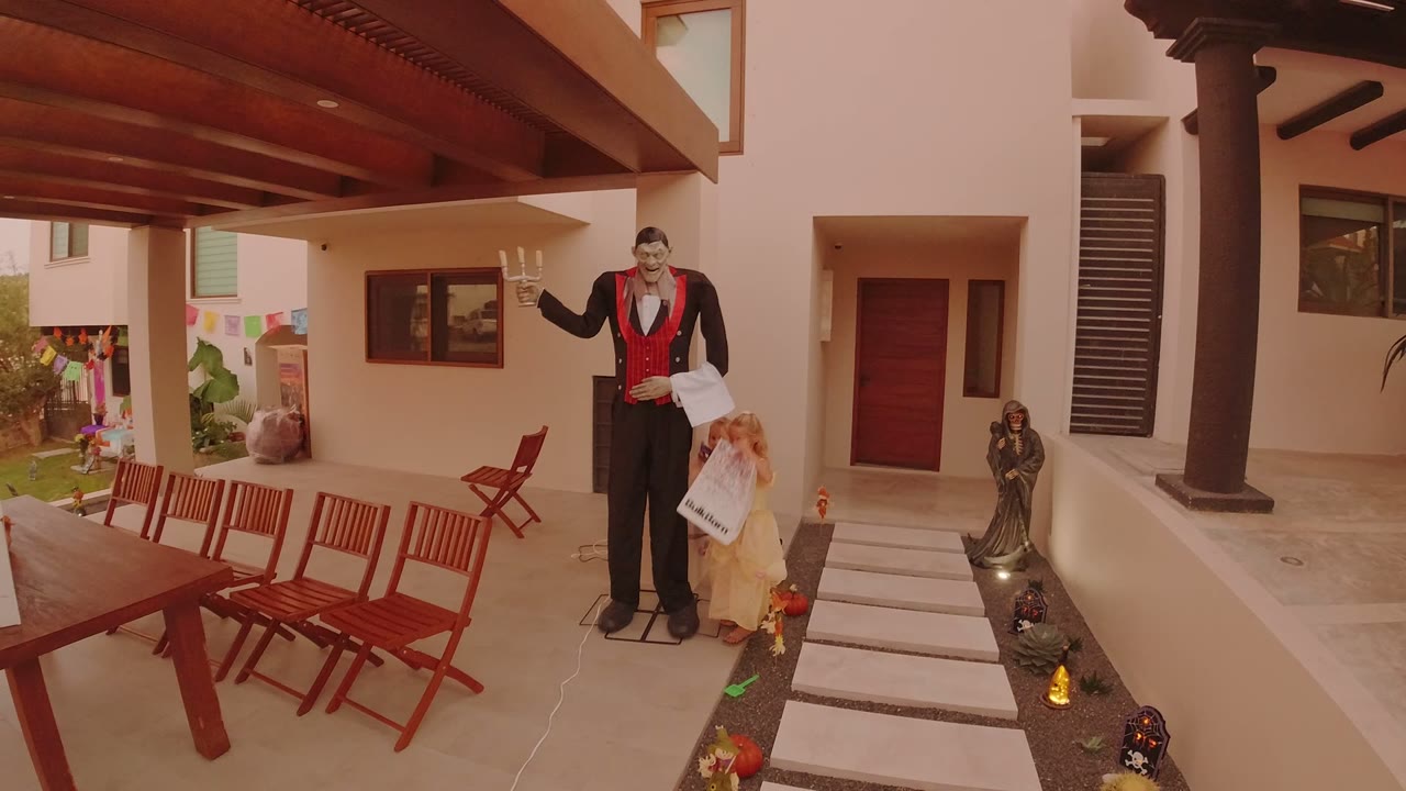The children remain beside the tall holiday figure on the Los Cabos patio, with red dining chairs to the left and small decorations lining the walkway.