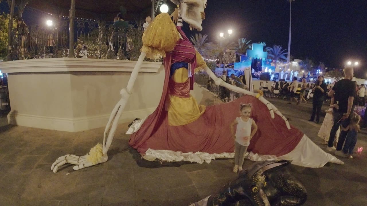 Child stands near a giant skeleton sculpture at night.