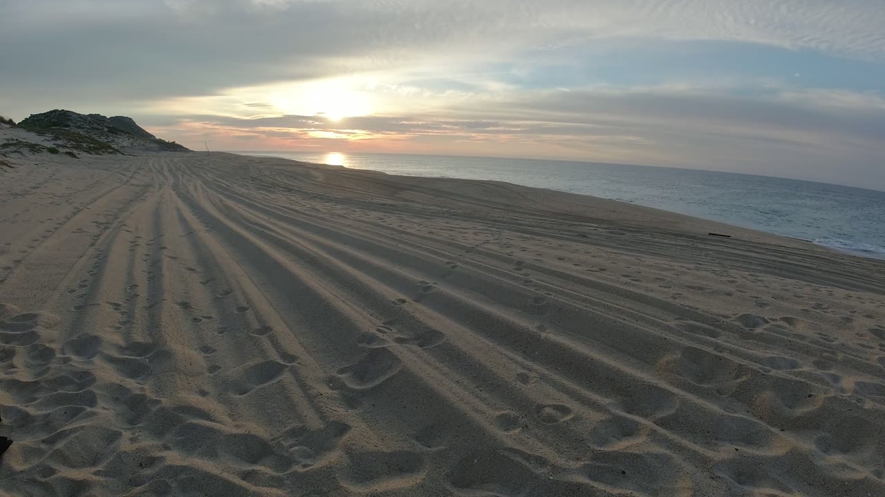 Raked beach sand leading toward sunset over the ocean.