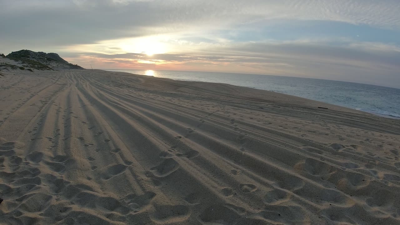 Ridged sand on a Los Cabos beach points toward the horizon while the sun sits above the water and no visible people appear in frame.