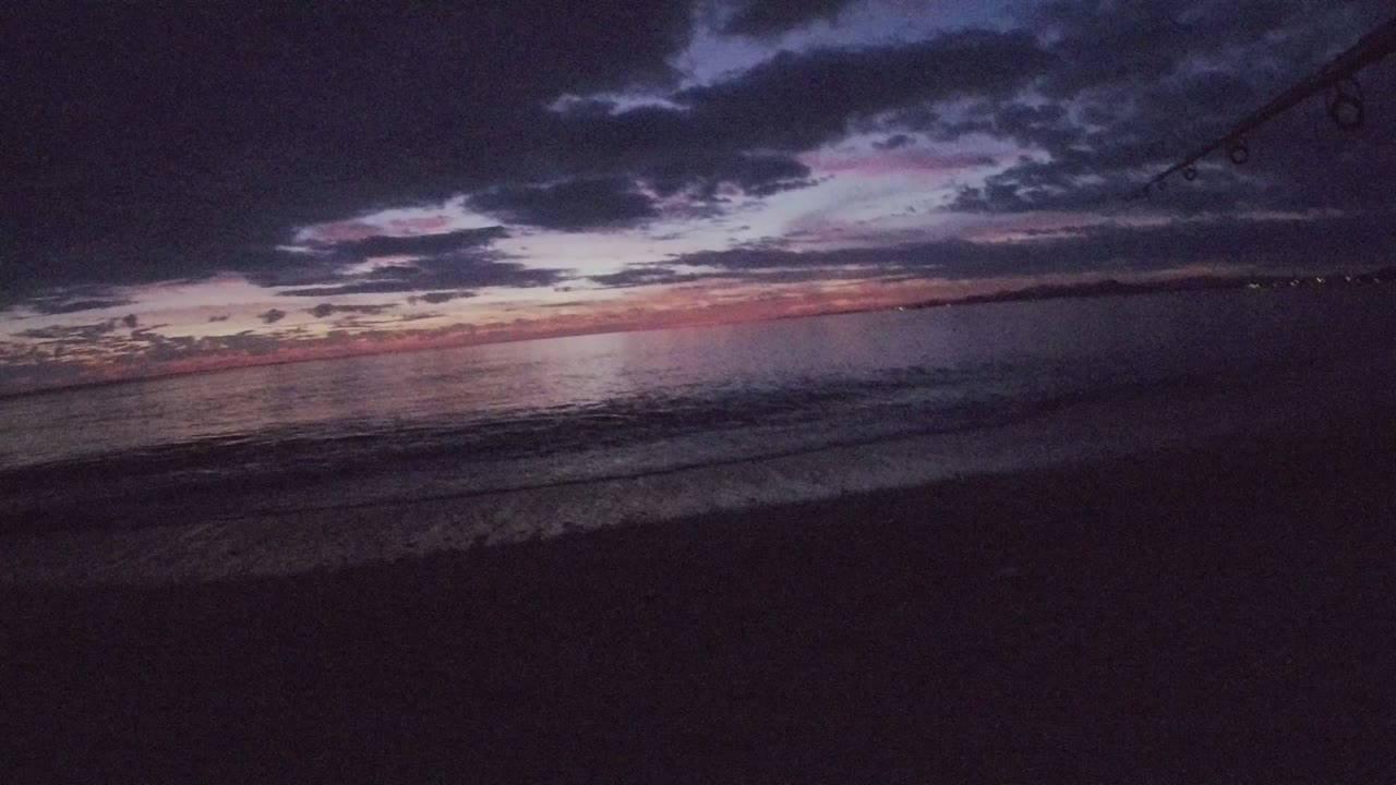 Dark beach and calm sea under a purple-orange dusk sky.