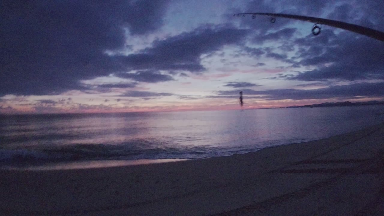 Sunset shoreline with fishing rod at top edge and small figure near the water