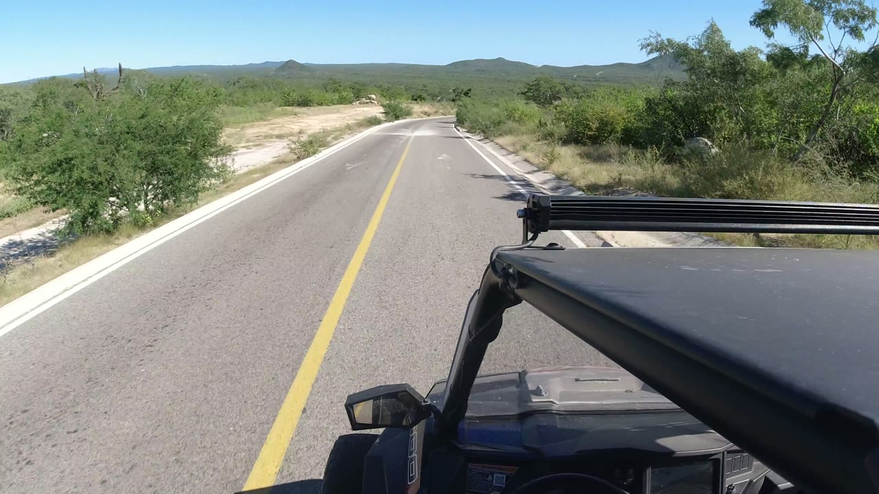 Jeep hood and light bar on a paved road through dry scrub hills.