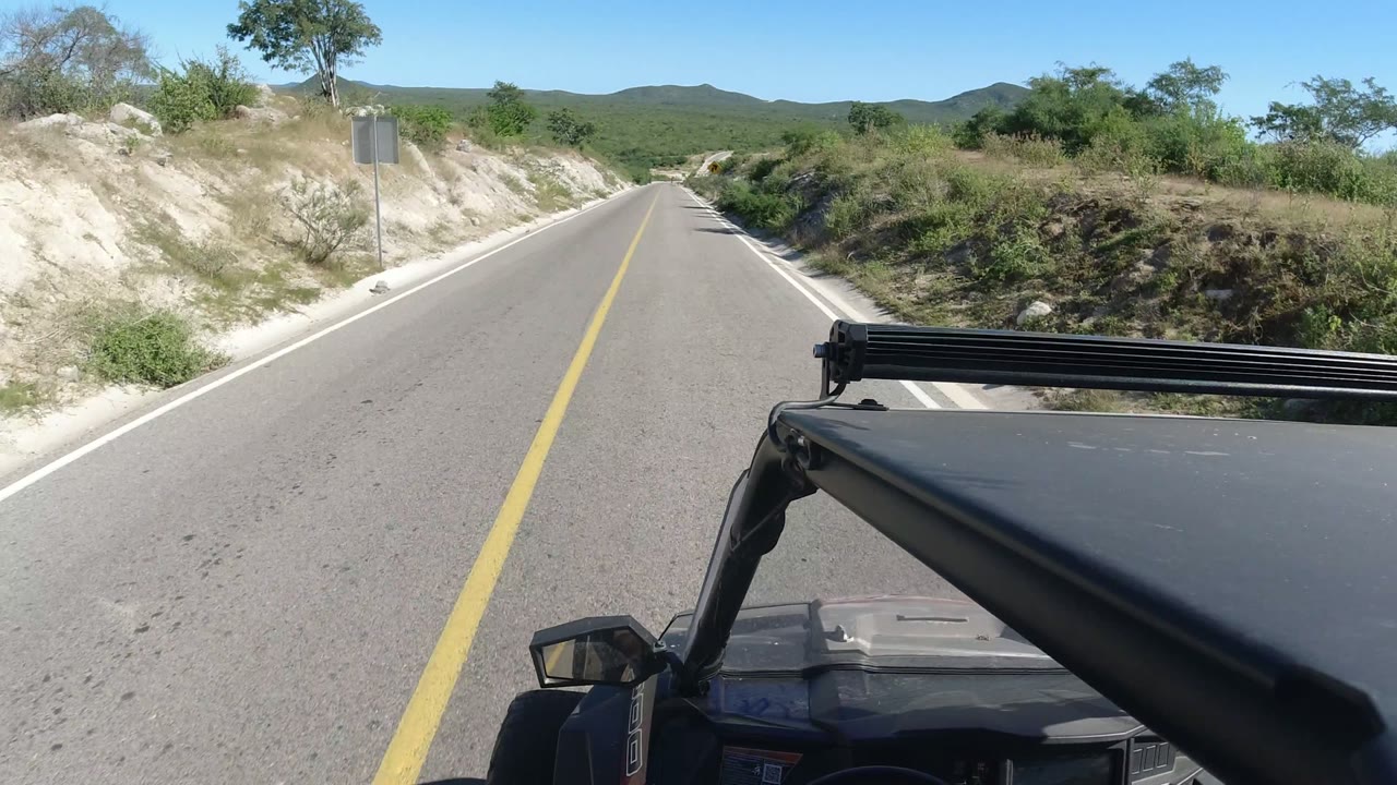 Vehicle view down a paved road through sandy terrain