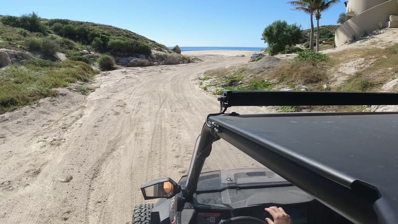 Off-road vehicle roof frame on a sandy road leading toward the ocean.