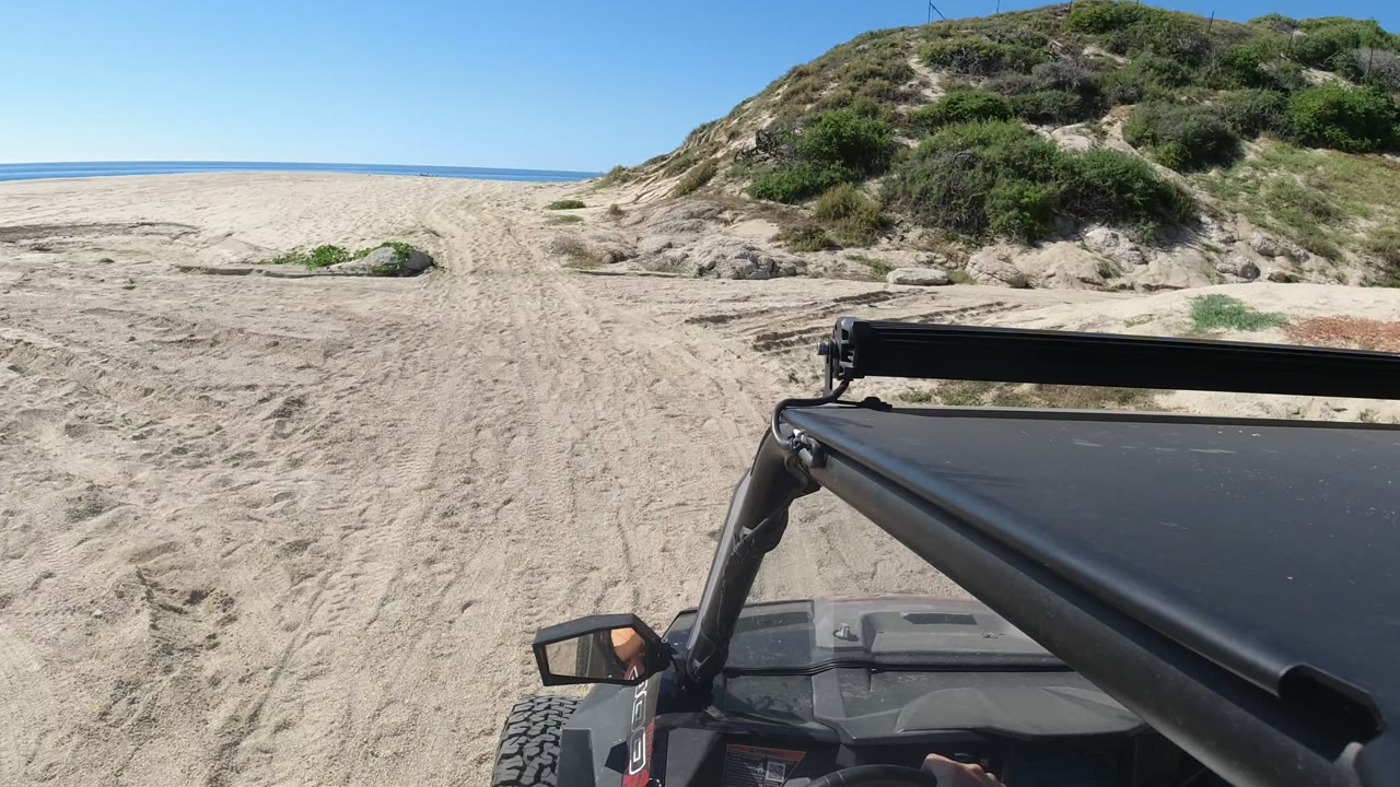 Jeep hood and roll bar on a sandy beach road beside dunes and ocean.