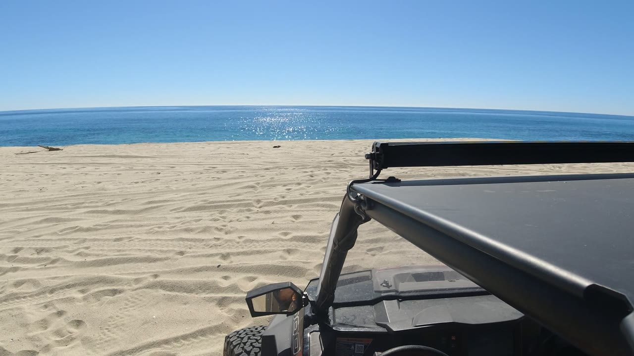 Open off-road vehicle beside a sandy beach and blue ocean.