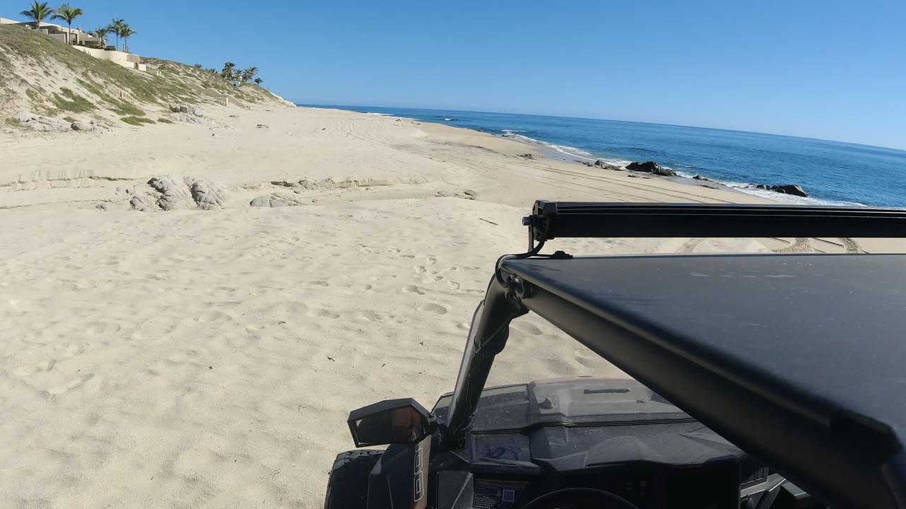 Off-road truck on sandy beach beside blue ocean and dunes