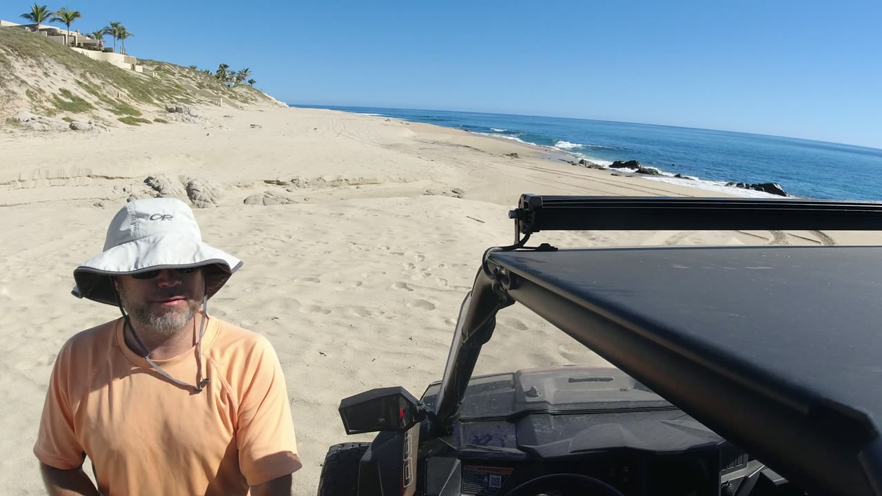 Man in sun hat beside an off-road vehicle on a sandy beach