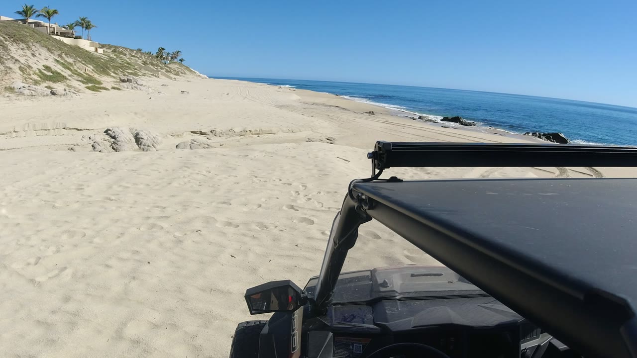 Off-road vehicle parked on sand beside a bright blue shoreline.