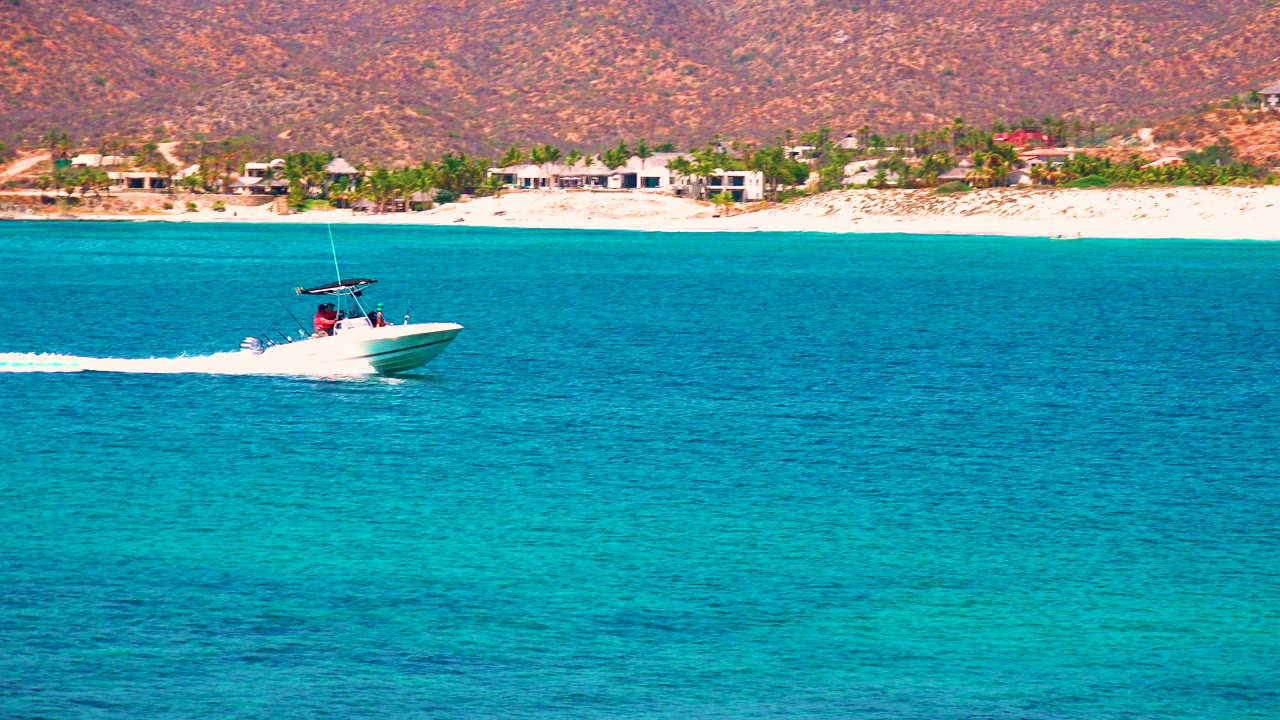 Motorboat farther right on turquoise water with beach and hills behind.