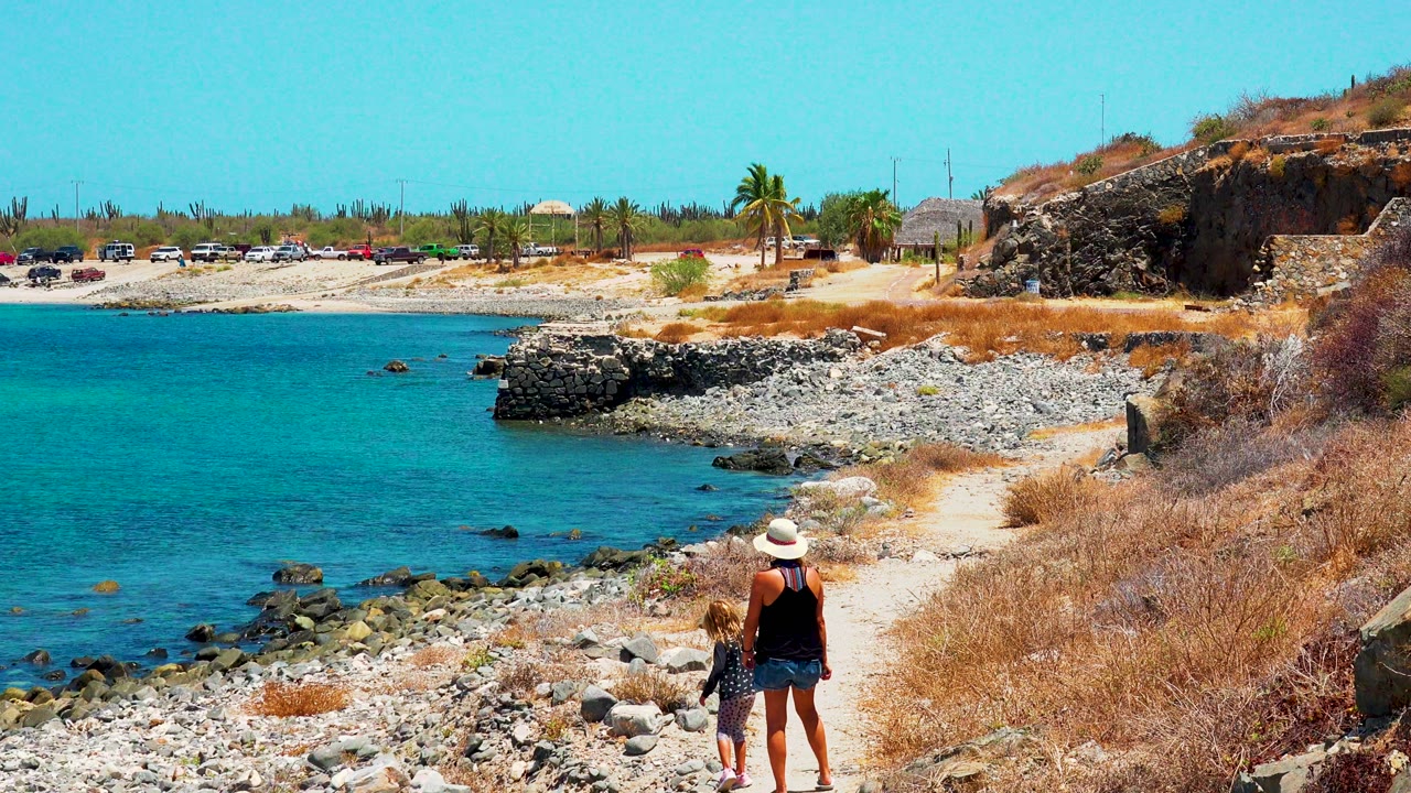 Woman watches a child and dog on a rocky beach path.