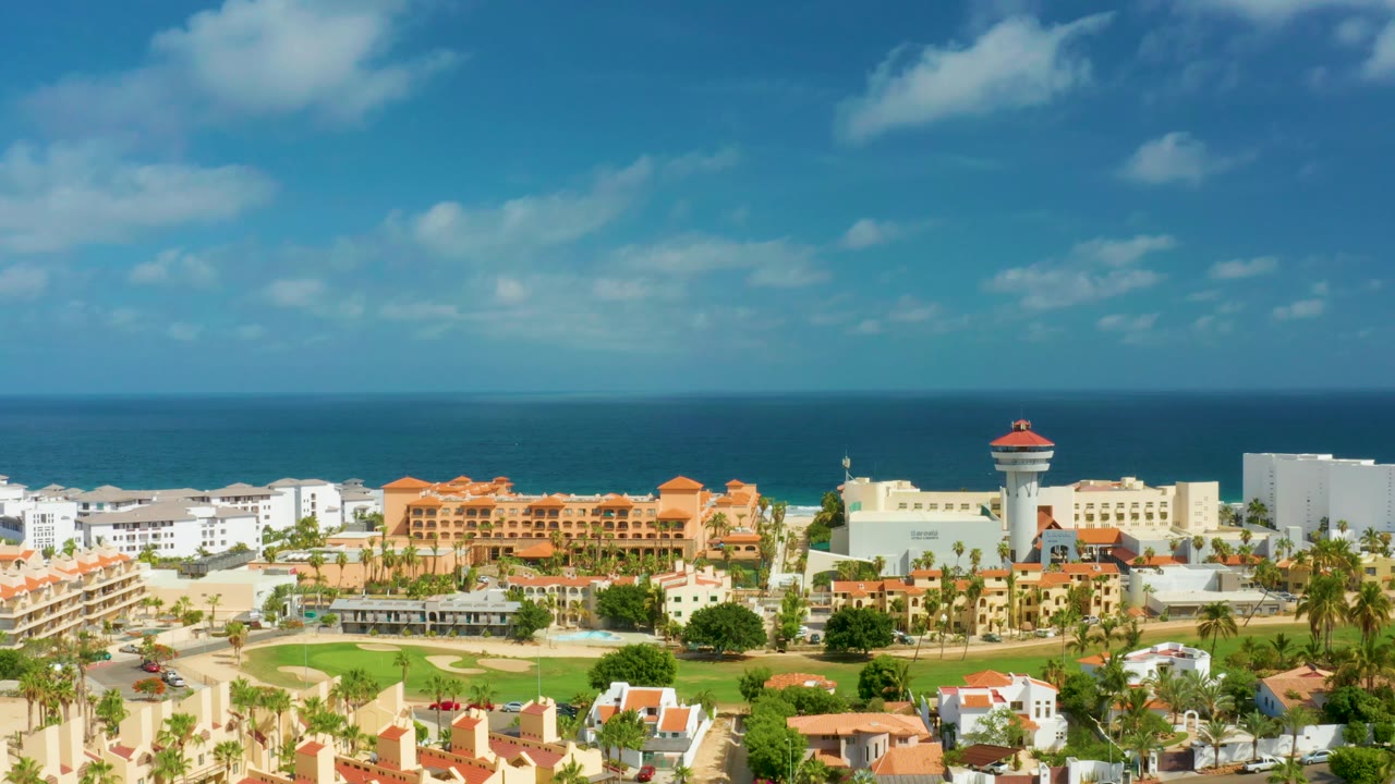San Jose Del Cabo, Mexico appears in a broad aerial composition with ocean beyond the buildings and a large blue sky overhead, no visible people.