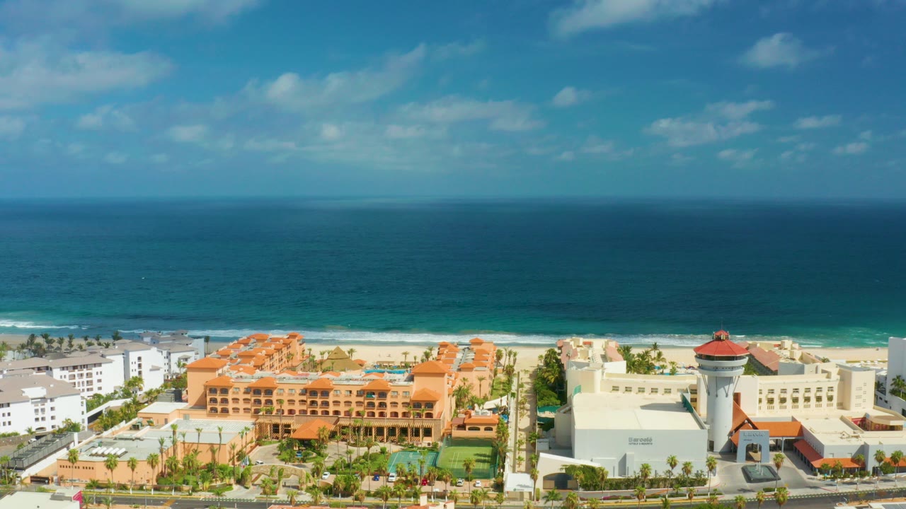 Aerial view in San Jose Del Cabo, Mexico showing blue ocean, a sandy beach, orange-roofed resort buildings, white hotel blocks, palms, and no visible people.