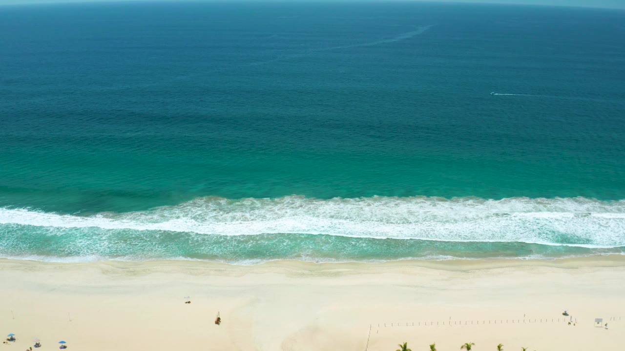 Aerial shoreline view with white waves crossing turquoise water and sand.