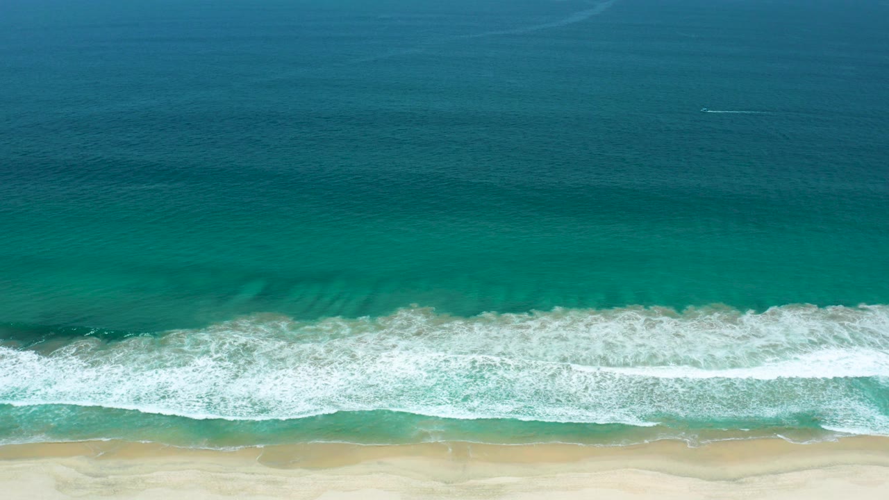 Overhead teal water and white surf reaching a sandy beach.