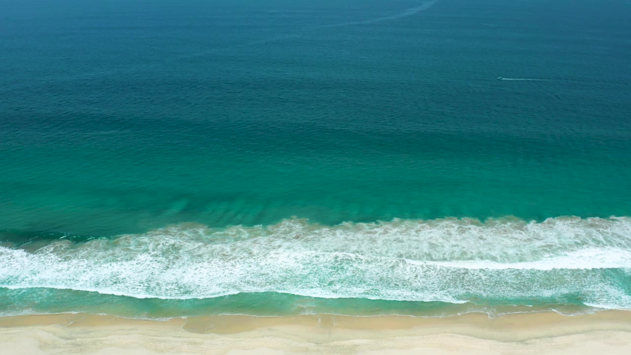 A wider band of white foam spreads through shallow turquoise water toward the sand in San Jose Del Cabo, Mexico, with no visible people.