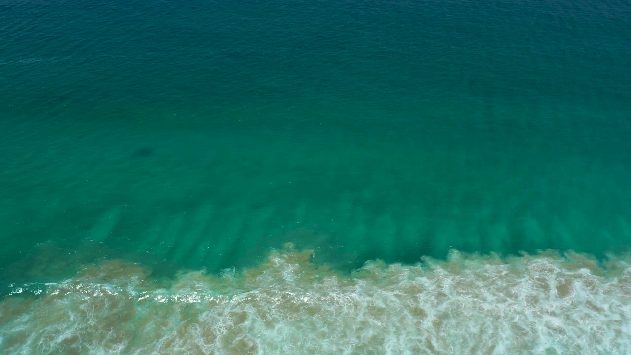 Top-down San Jose Del Cabo shoreline view with open green sea occupying most of the frame and white surf touching sand at the bottom, no visible people.