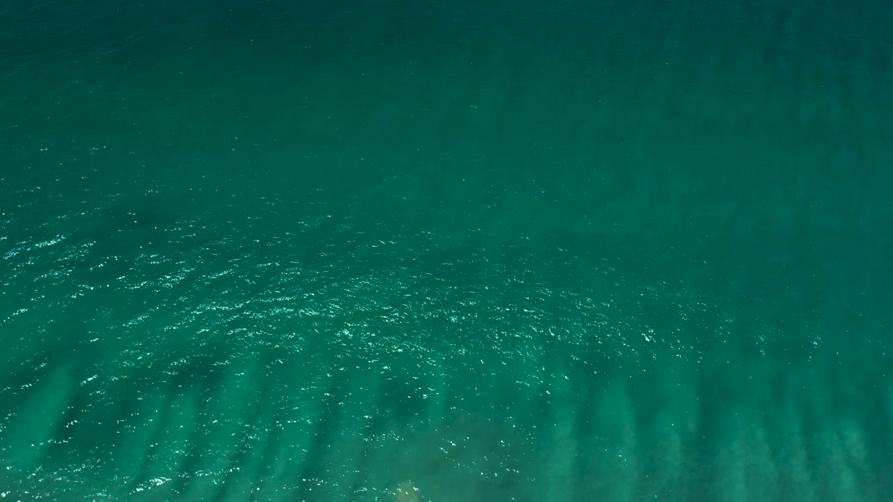 Top-down view of deep turquoise seawater in San Jose del Cabo with brighter ripples across the right side and no visible people.
