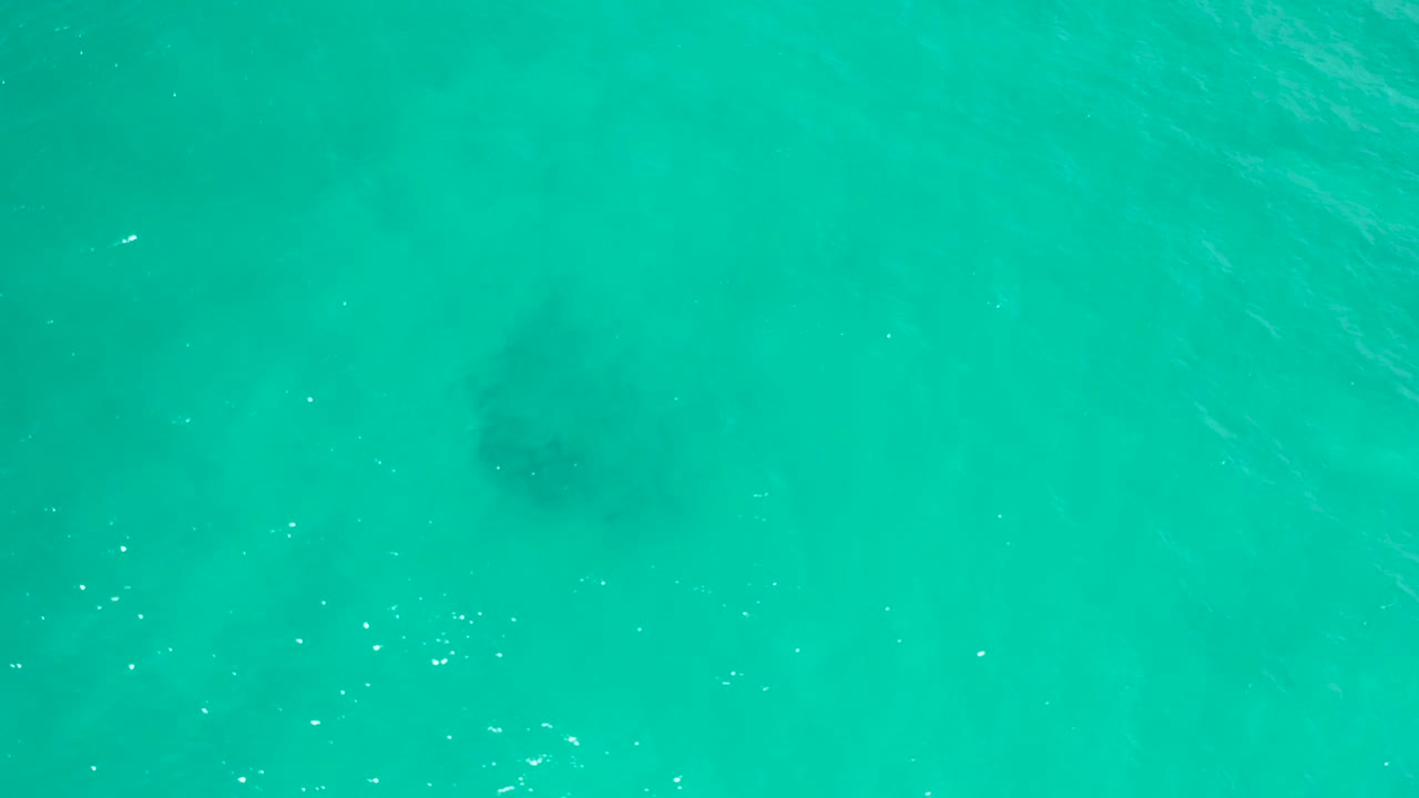 Aerial-looking frame of San Jose Del Cabo turquoise water with a soft dark patch under the surface near center-left and no visible people.