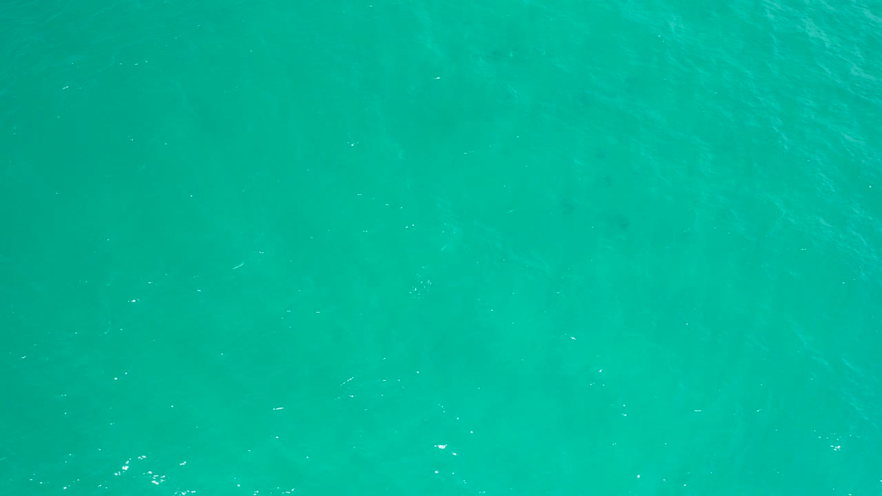 Overhead view of turquoise ocean water in San Jose Del Cabo with faint submerged patches, light surface ripples, and no visible people.