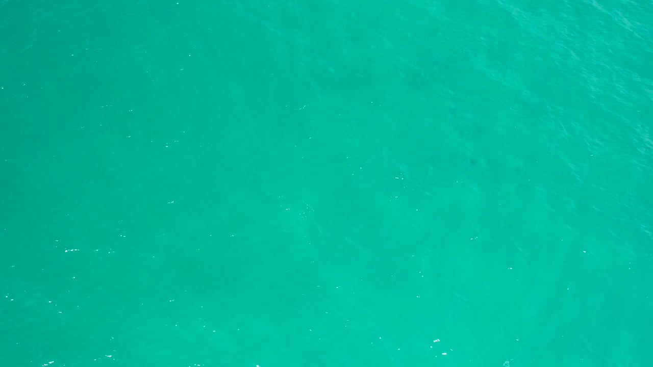 Clear turquoise sea in San Jose Del Cabo shows darker shapes below the surface and scattered white glints, with no visible people.