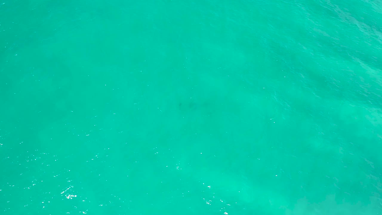 Clear blue-green water with faint underwater shapes