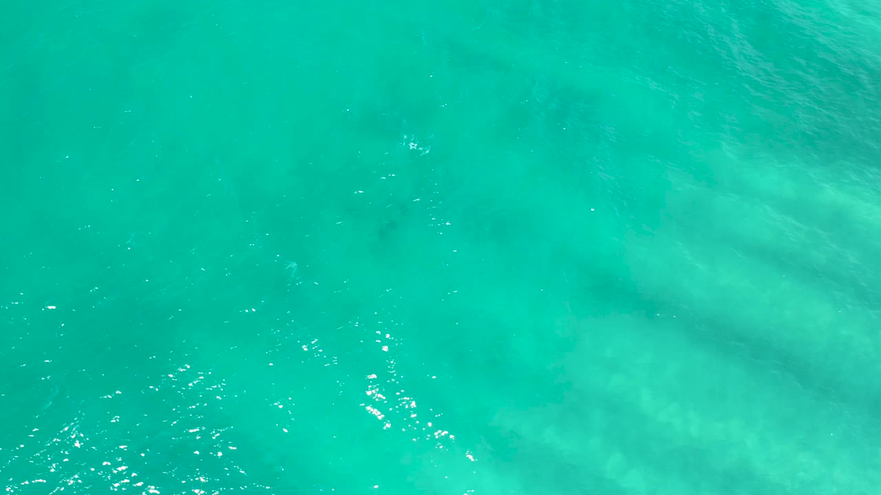Aerial view of turquoise water in San Jose Del Cabo with darker subsurface patches and light ripples, with no visible people.