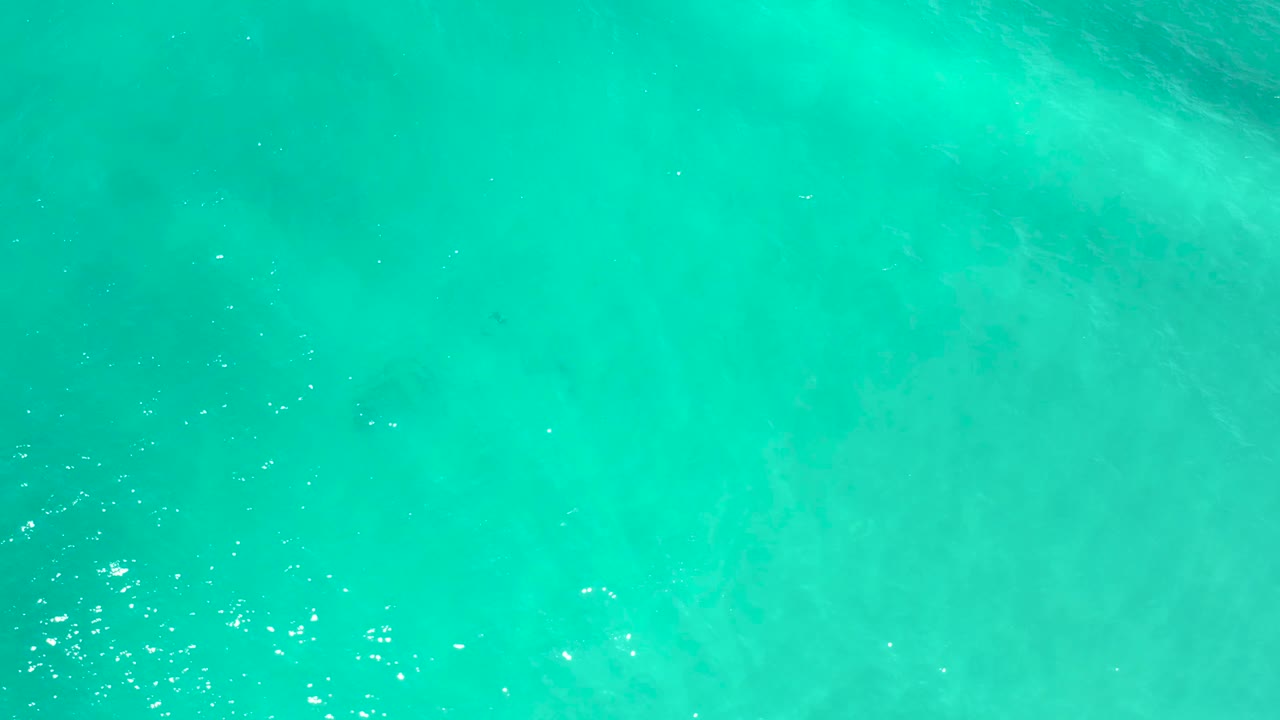 Overhead San Jose del Cabo water frame showing green-blue ocean, scattered white reflected highlights, soft ripples, and no visible people.