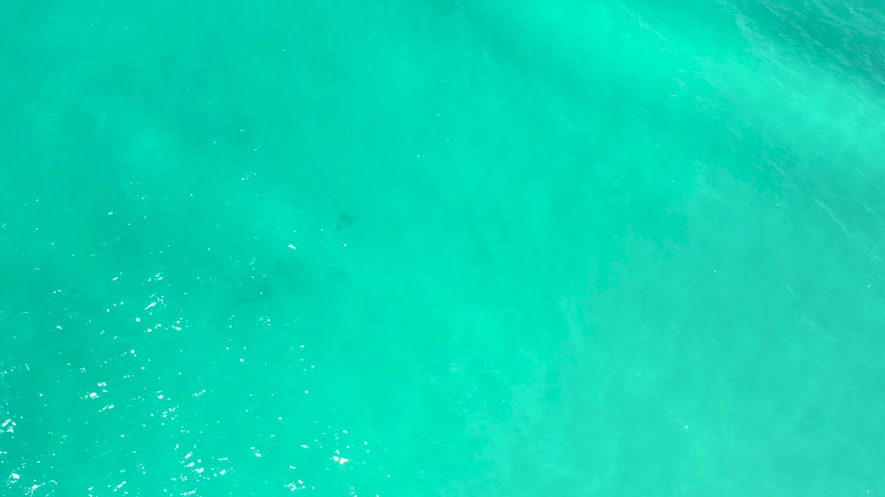 Top-down turquoise ocean in San Jose del Cabo, Mexico, with a brighter rippled area near the middle, diffuse pale shapes beneath the water, and no visible people.