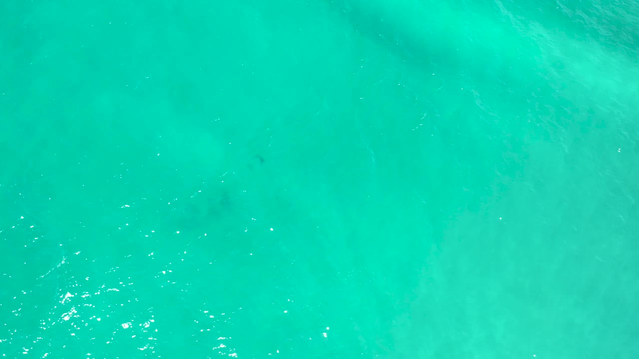 Overhead view of teal-green San Jose del Cabo ocean water with soft diagonal haze beneath the surface, sparse white sparkle, and no visible people.