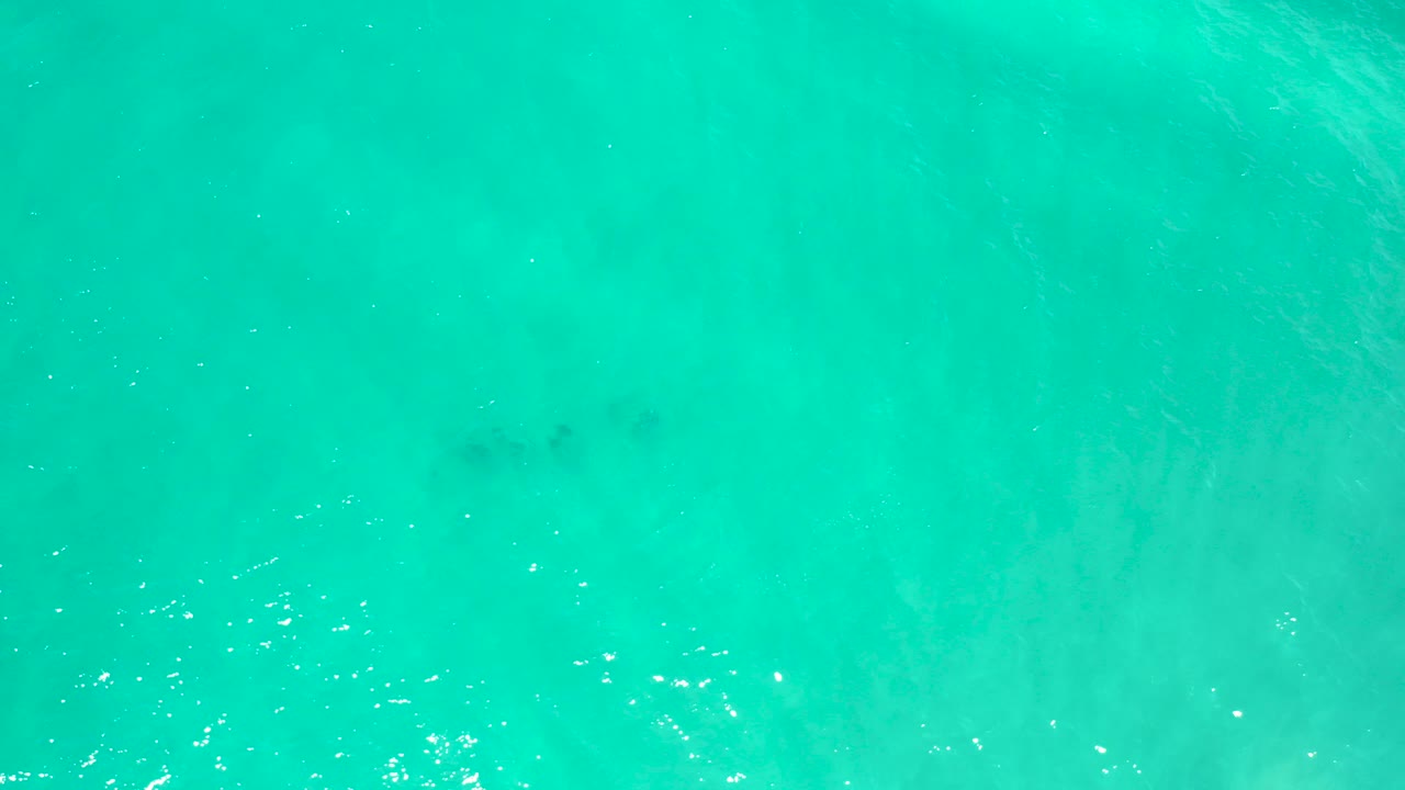 Top-down cyan ocean water with faint darker patches and sun glints.