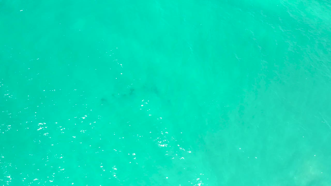 Cyan sea surface in San Jose Del Cabo, Mexico, with a small darker blurred patch beneath the water and no visible people.
