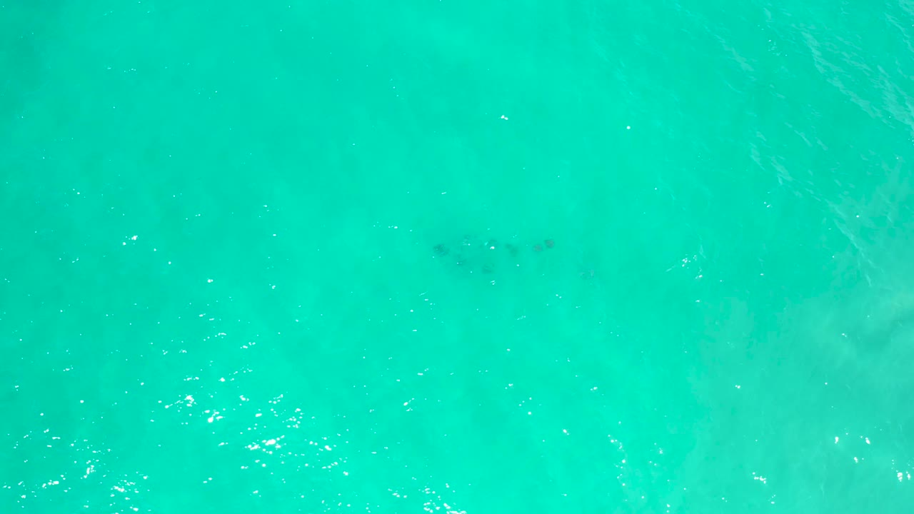 Aqua sea surface in San Jose Del Cabo, Mexico, showing scattered white highlights and faint darker underwater patches, with no visible people.
