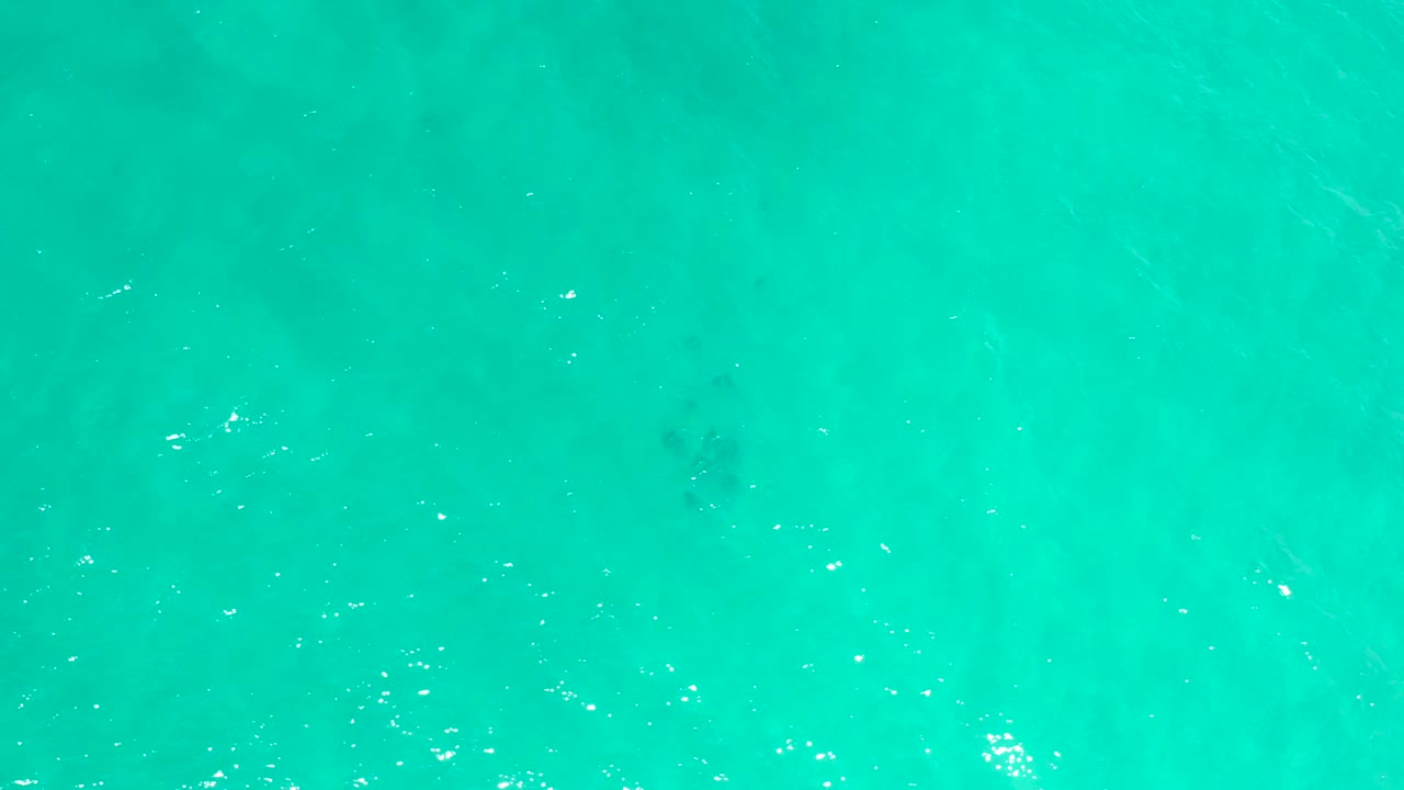 Green-blue sea surface in San Jose Del Cabo, Mexico, with scattered sunlight highlights and faint darker patches below, no visible people.