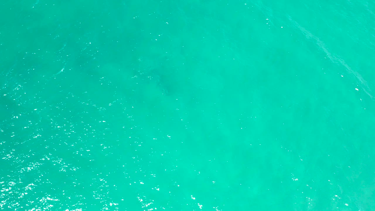 Overhead view of turquoise water in San Jose del Cabo with faint pale patches under the surface, scattered white reflections, and no visible people.