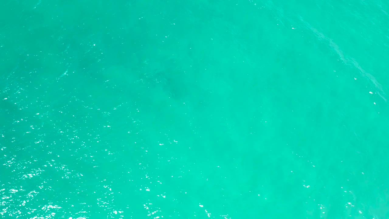 Aqua ocean water in San Jose del Cabo fills the frame with soft ripples, bright surface specks, a faint darker area below, and no visible people.