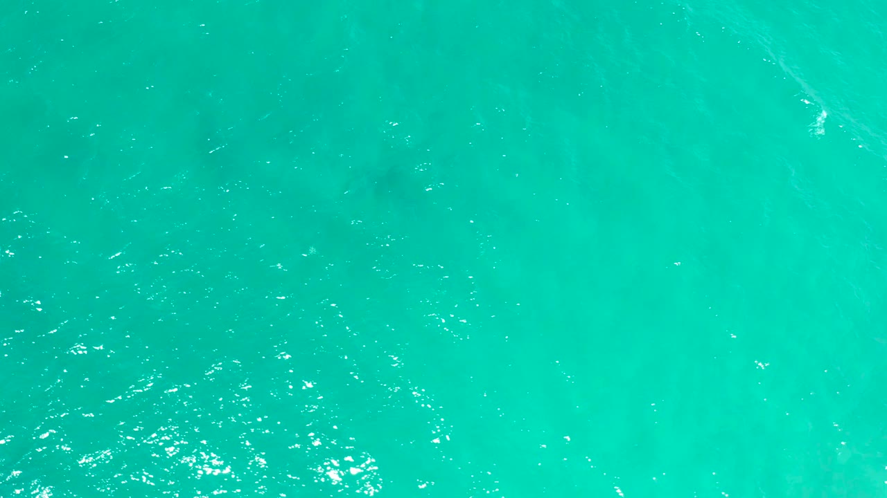 Clear turquoise water in San Jose del Cabo shows scattered sparkle, gentle wave marks, mottled depth changes below the surface, and no visible people.