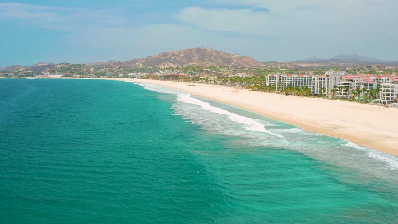 Aerial beach view with white surf bands and resorts below dry hills.