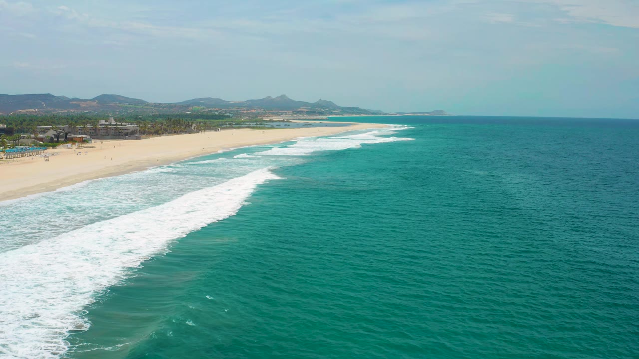 Wide coastline with green-blue water and white surf beside sand.