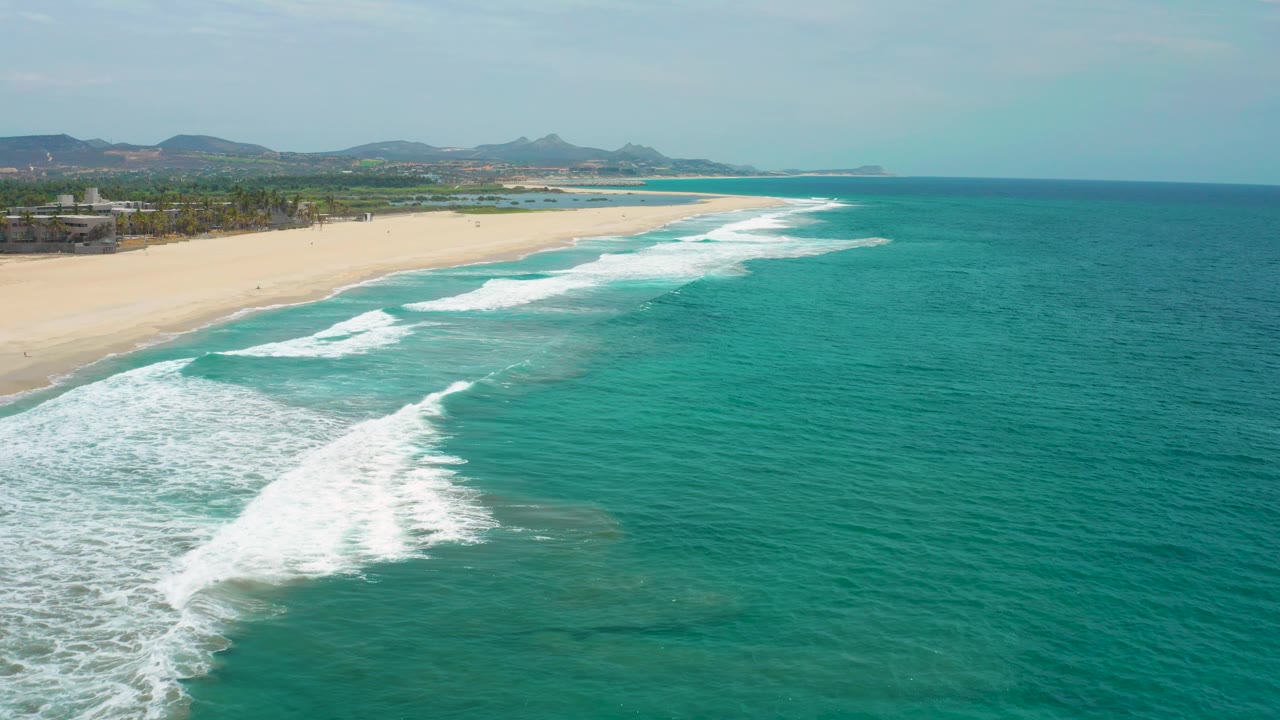 At three seconds, a larger white foam patch spreads in the lower left while the empty San Jose del Cabo beach arcs into the distance beside clear turquoise water, with no visible people.