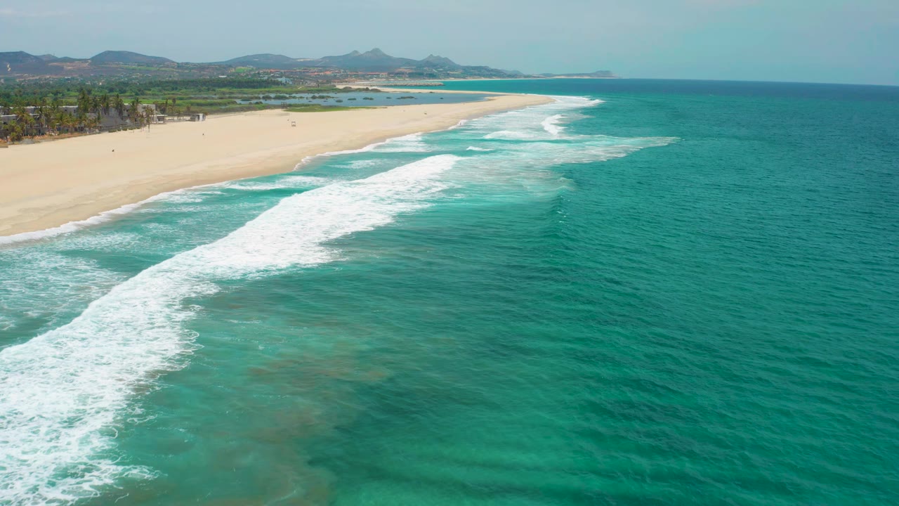 White surf bands roll diagonally toward an empty sandy shoreline.