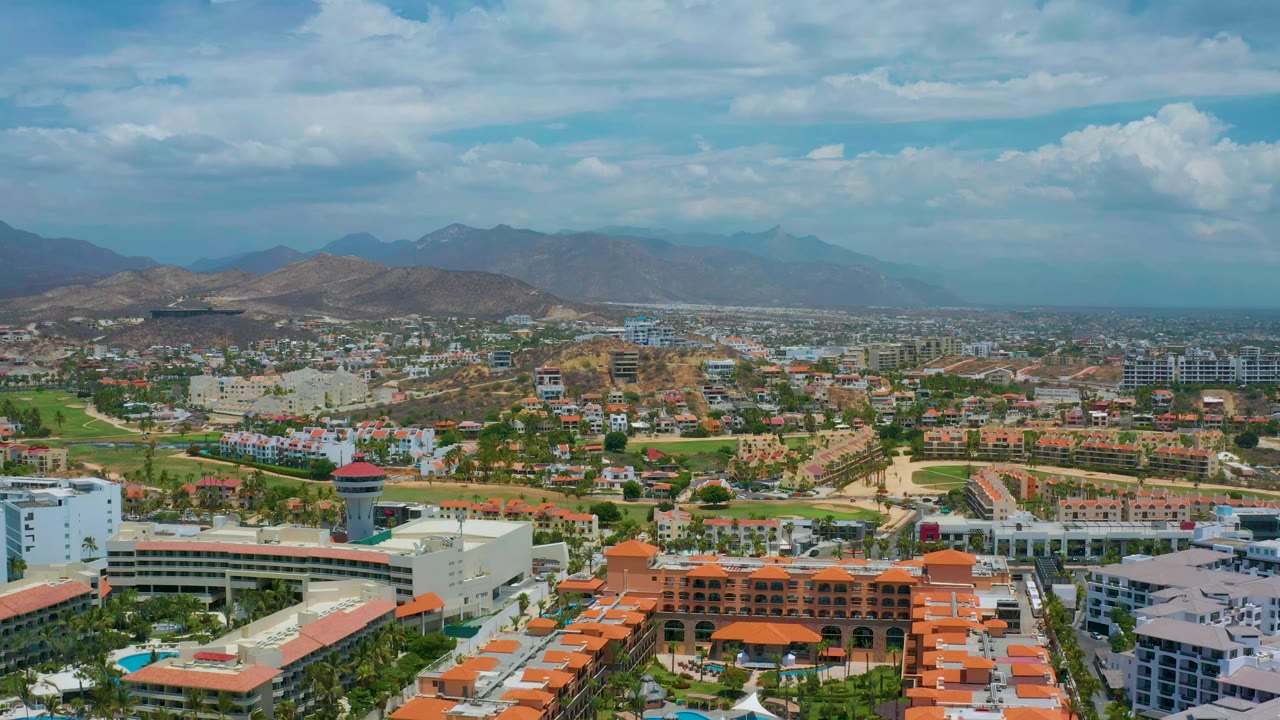 Wide aerial resort view with orange roofs, green areas, roads, and mountains.