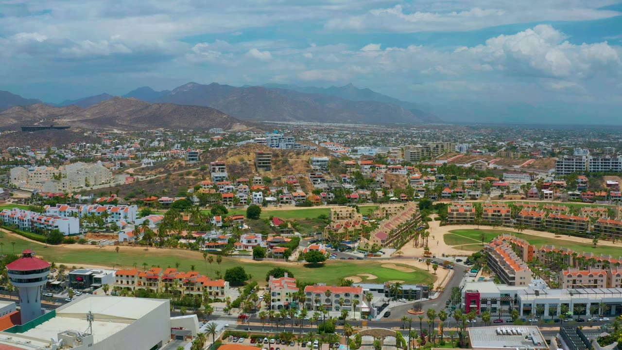 Aerial town view with resort-style buildings, roads, green space, hills, and distant mountains.