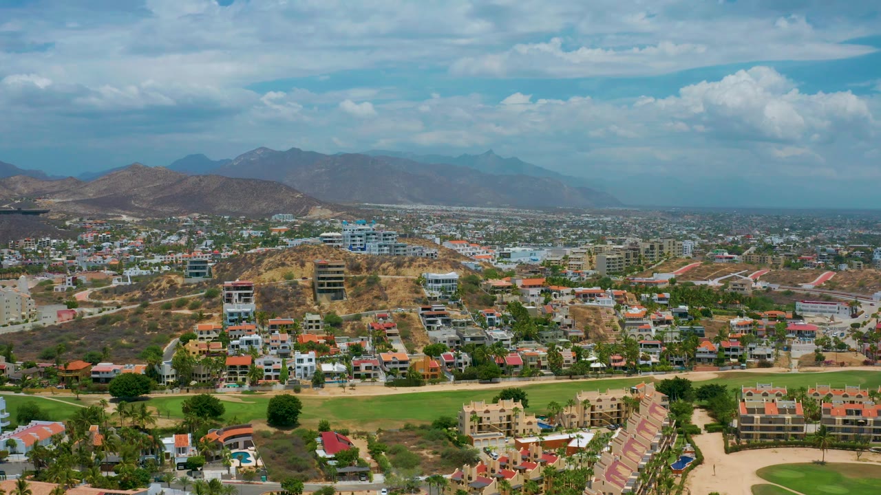 Aerial view across houses and buildings toward hazy mountains and clouds.