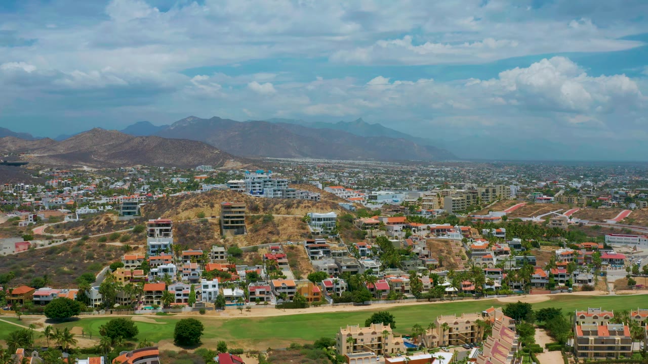 Aerial view across residential buildings and hills toward hazy mountains.
