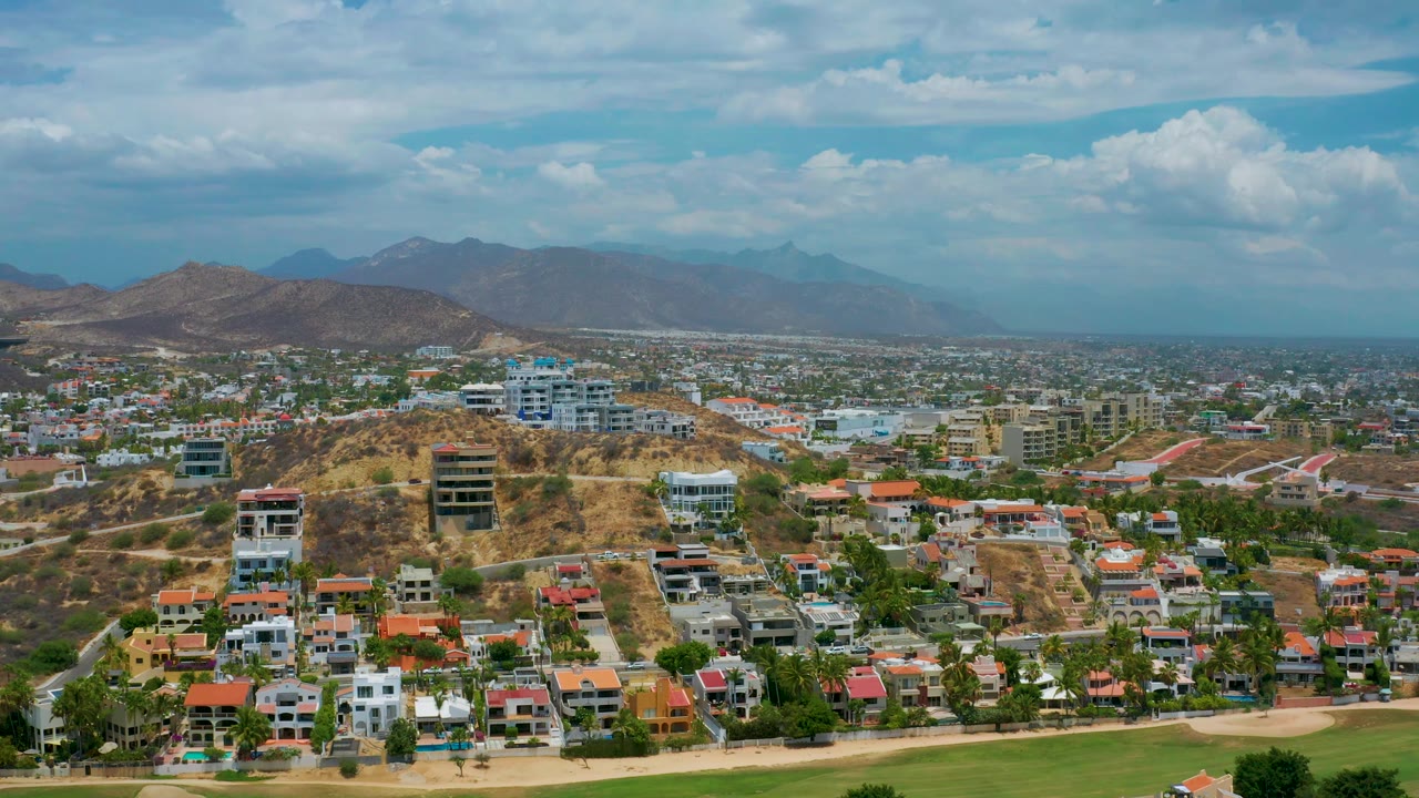Wide aerial over residential blocks, hillside construction, and mountains.