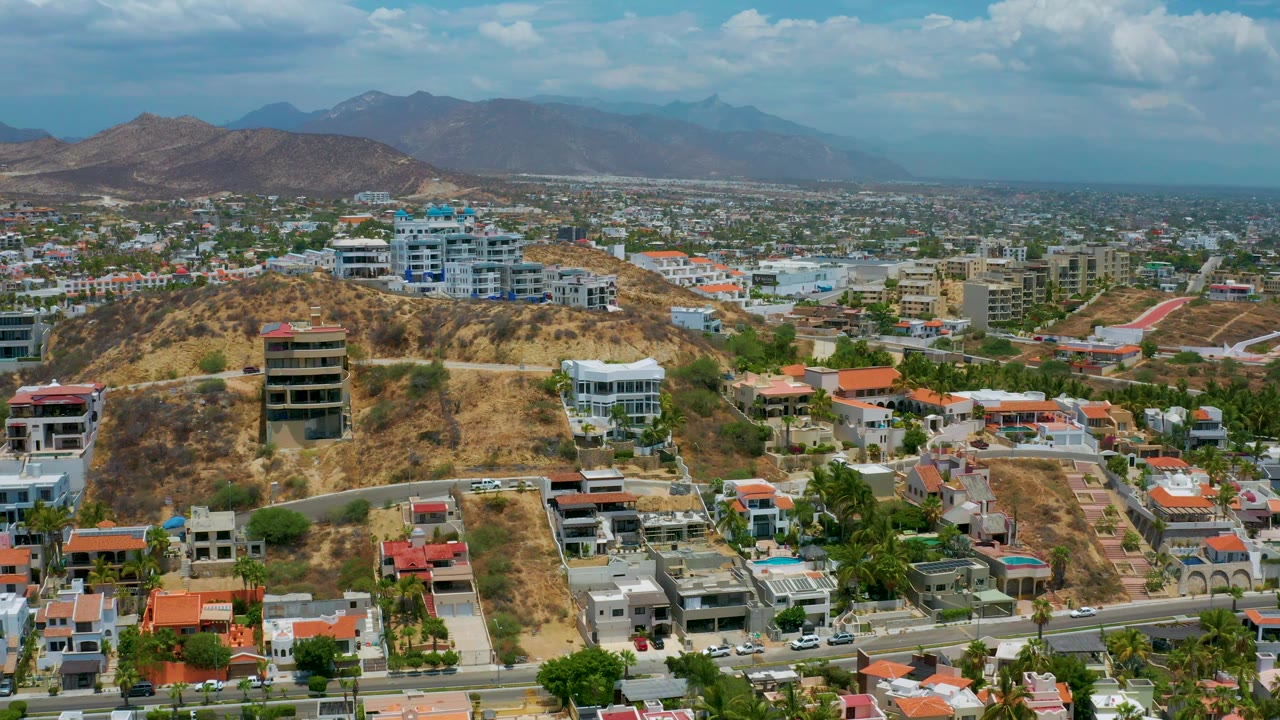 Aerial view of a dry hillside with homes, mid-rise buildings, and mountains.