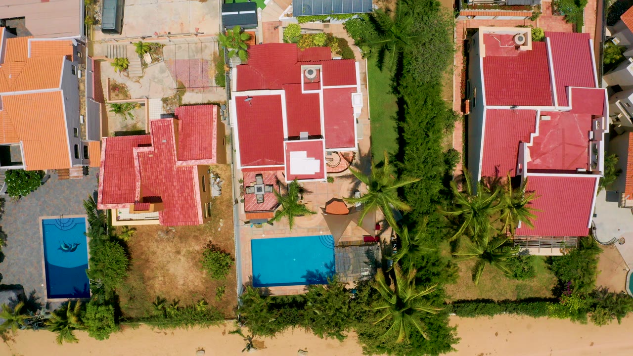 Top-down aerial view in San Jose Del Cabo, Mexico showing red-roofed private homes, blue pools, palms, tan yards, and no visible people at the start of the clip.